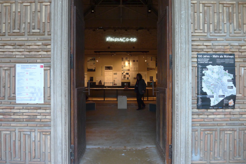 The entrance of the Greek Pavilion with the poster of the workshop on the one side and the map of all Zurich's housing cooperatives on the other side